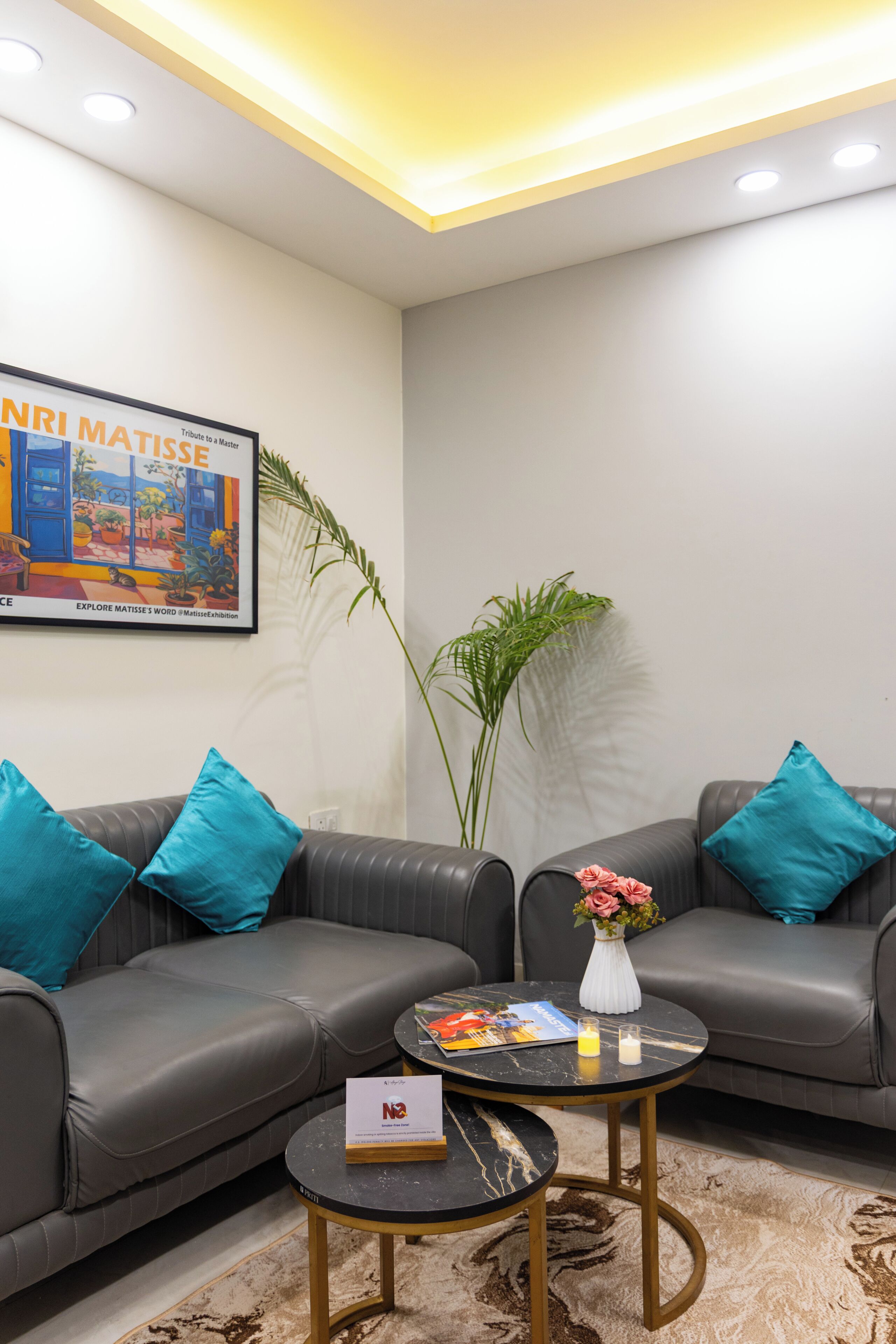 A modern living room with two grey sofas, a black coffee table, a framed artwork, and a potted plant.