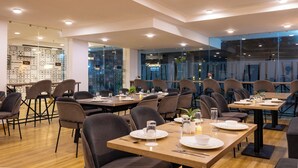 A modern restaurant with tables set for dining, large windows, and a view of the cityscape.