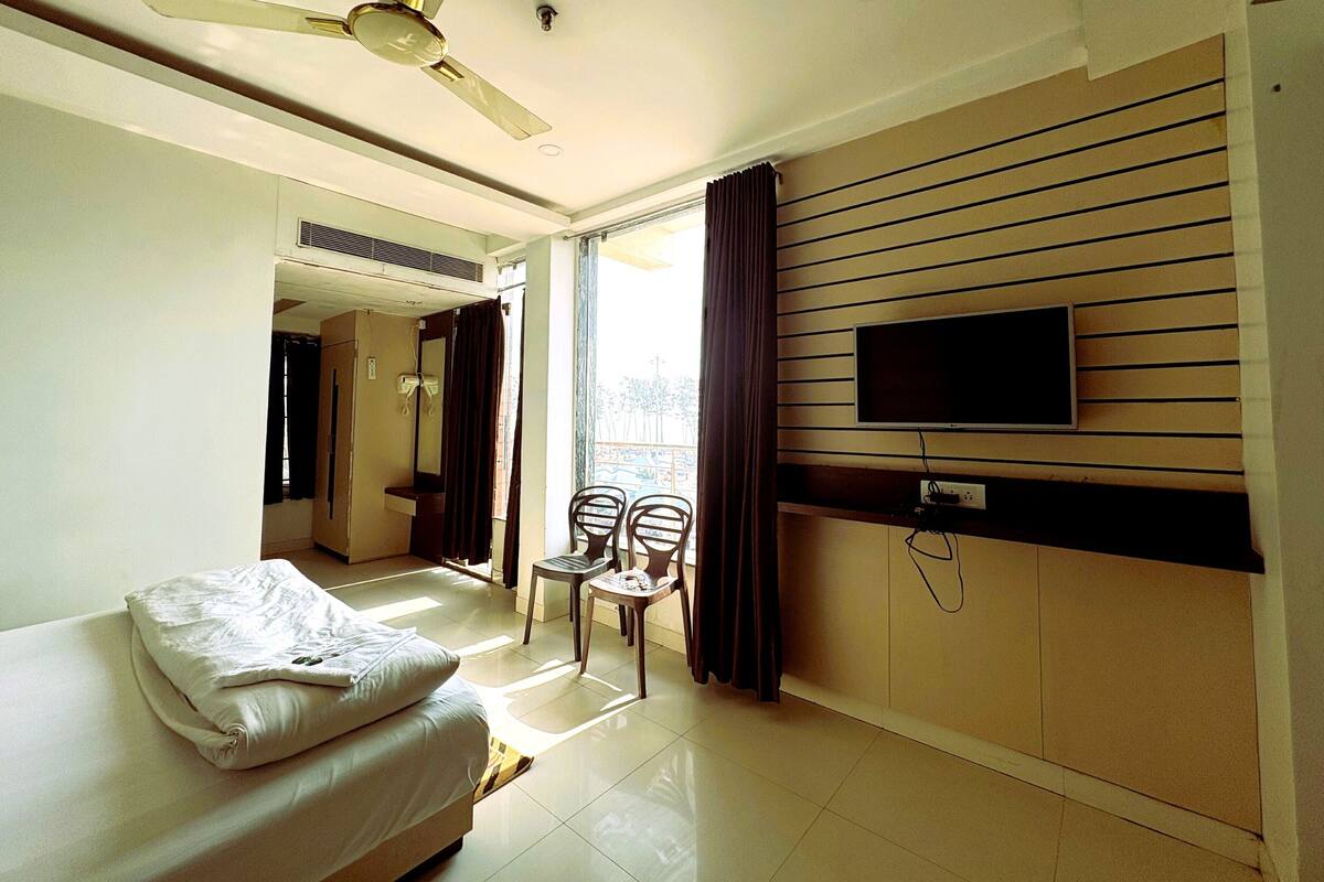 A hotel room with a bed, a ceiling fan, a TV, a window with curtains, and a bathroom visible through an open door.