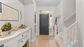 A hallway with a white console table, a map, a door, and a staircase. - Marsh Breeze Hideaway at Masters Place (Pawleys Island)
