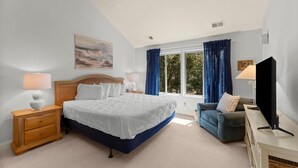 A bedroom with a bed, bedside tables, a TV, a ceiling fan, and a window with curtains. - Marsh Breeze Hideaway at Masters Place (Pawleys Island)