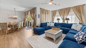 A living room with a blue sofa, a coffee table, and a dining area with a wooden table and chairs. - Marsh Breeze Hideaway at Masters Place (Pawleys Island)