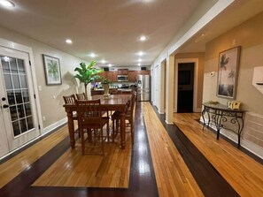 A spacious kitchen with wooden flooring, a dining area with a table and chairs, and a small side table with a lamp. - A comfy stay close to the beach! Bike&Pet Friendly (Horry County)