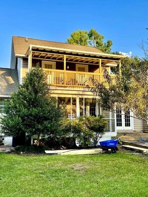 A two-story house with a covered porch, a lawn, and a blue wheelbarrow. - A comfy stay close to the beach! Bike&Pet Friendly (Horry County)