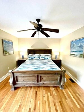 A bedroom with a bed, a ceiling fan, two bedside lamps, and two wall-mounted paintings. - A comfy stay close to the beach! Bike&Pet Friendly (Horry County)