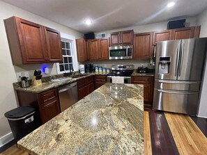 Una cocina con gabinetes de madera, encimera de granito, electrodomésticos de acero inoxidable y un cubo de basura.