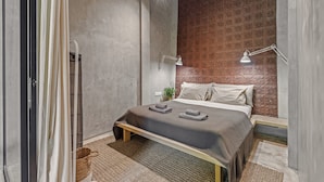 Une chambre moderne avec un lit, des lampes de chevet, une petite plante et un mur à texture.