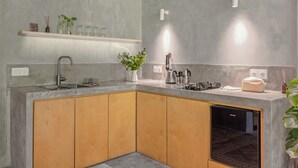 A modern kitchen with a built-in dishwasher, wooden cabinets, a countertop with various appliances, and a shelf with decorative items. - Pager Apartments 2BR in Ubud Center (Ubud)