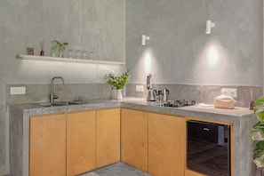 A modern kitchen with a built-in dishwasher, wooden cabinets, a countertop with various appliances, and a shelf with decorative items. - Pager Apartments 2BR in Ubud Center (Ubud)