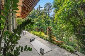 Tapete de yoga e halteres em um pátio de concreto com vista para vegetação exuberante e uma estrutura de madeira.