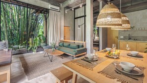 A modern living room with a sofa, dining table, and a large window with bamboo plants. - Pager Apartments 2BR in Ubud Center (Ubud)