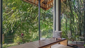 A modern room with a large window, a wooden bench, and a view of dense greenery. - Pager Apartments 2BR in Ubud Center (Ubud)