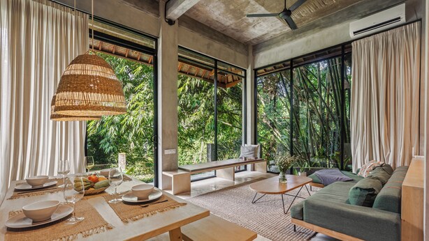 A modern interior with a dining area, a sofa, and large windows overlooking greenery. - Pager Apartments 2BR in Ubud Center (Ubud)