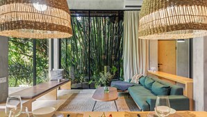 A modern room with a sofa, dining table, and a view of greenery through large windows. - Pager Apartments 2BR in Ubud Center (Ubud)
