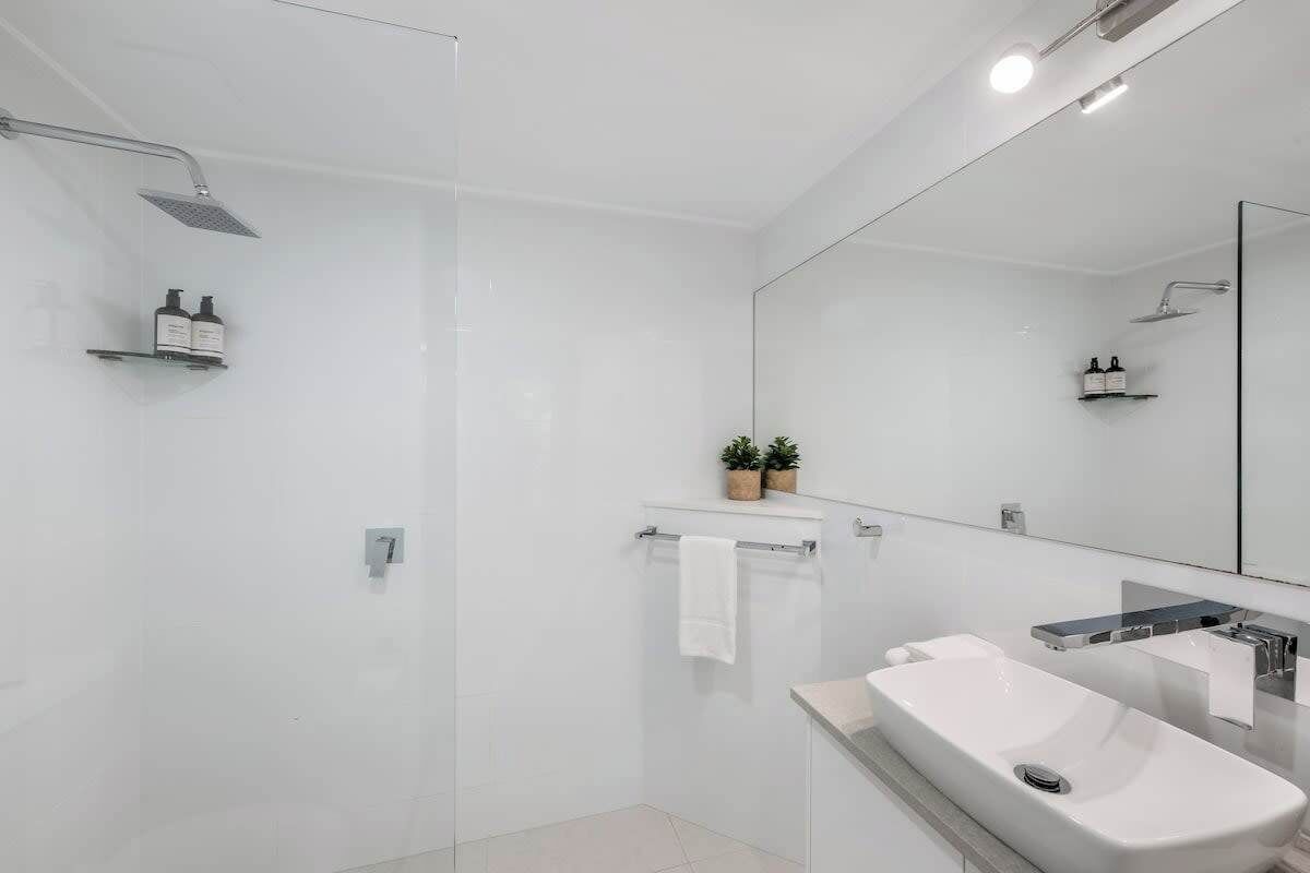 Ein modernes Badezimmer mit einer Duschkabine aus Glas, einem großen Spiegel und einem weißen Waschbecken.