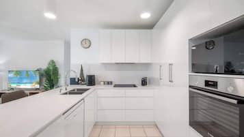 A modern kitchen with white cabinetry, a Bosch oven, a clock, and a television displaying a beach scene.
