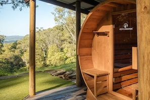 A wooden sauna with a logo, a bench, and a view of a forested landscape. - Rhulani Lodge ~ sauna, spa, pizza oven, fireplace (Eudlo)