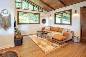 A cozy living room with a sofa, coffee table, and large windows. - Rhulani Lodge ~ sauna, spa, pizza oven, fireplace (Eudlo)