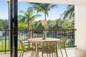 Ein Balkon mit Tisch und Stühlen und Blick auf einen Golfplatz sowie Palmen.