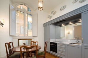 A dining area with a round table and chairs, a window with shutters, and a kitchen with grey cabinets and a sink. - House Bardi Florence (Firenze)