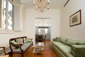 Een woonkamer met een bank, een salontafel, een kroonluchter, en een eethoek met stoelen en een tafel.