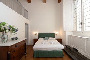 A bedroom with a bed, bedside tables, a dresser, a vase with flowers, a window with a view, and a staircase. - House Bardi Florence (Firenze)
