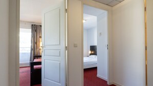 Ein Hotelzimmer mit rotem Teppich, einem Bett mit weißer Bettwäsche, einem Nachttisch und einem Fenster mit Vorhängen.