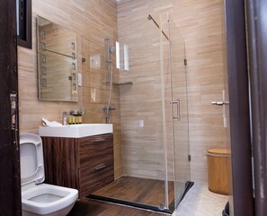 A modern bathroom with a glass shower enclosure, a white sink, and a wooden vanity. - Fallsway Palms (Lusaka)