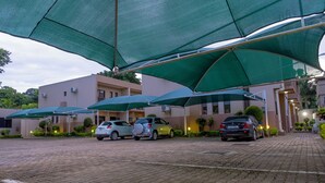 Ein Parkplatz mit Autos, beschattet von großen grünen Sonnenschirmen, und ein Gebäudeeingang mit sandfarbenem Mauerwerk.