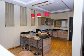 A modern kitchen with wooden cabinets, a central island with stools, and pendant lights. - Fallsway Palms (Lusaka)