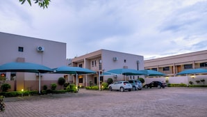 Ein Hotel mit einem gepflasterten Innenhof, mehreren parkenden Autos und grünen Sonnenschirmen, die Schatten spenden.