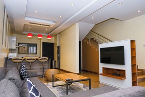 A modern living room with a sofa, coffee table, TV, and a staircase. - Fallsway Palms (Lusaka)