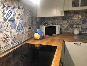Een keuken met patroon tegels, een magnetron en een blauw speeltje op het aanrecht.