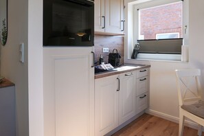 A kitchen with white cabinets, a black microwave, and a window with a view of a brick building. - Meeresleuchten - Sea lights on Sylt: relaxation, proximity to the beach & space for 4 (Wenningstedt-Braderup (Sylt))