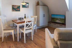A dining area with a table and chairs, a television, and a cabinet. - Meeresleuchten - Sea lights on Sylt: relaxation, proximity to the beach & space for 4 (Wenningstedt-Braderup (Sylt))