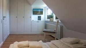 Ett sovrum med ett sluttande tak, en säng med hopvikta handdukar, en stol, ett element och en tv som är monterad på väggen.