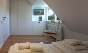 A bedroom with a sloped ceiling, a bed with folded towels, a chair, a radiator, and a TV mounted on the wall. - Meeresleuchten - Sea lights on Sylt: relaxation, proximity to the beach & space for 4 (Wenningstedt-Braderup (Sylt))