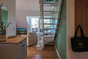 A modern interior with a wooden desk, a television, a staircase, and a view of the outdoors. - Meeresleuchten - Sea lights on Sylt: relaxation, proximity to the beach & space for 4 (Wenningstedt-Braderup (Sylt))