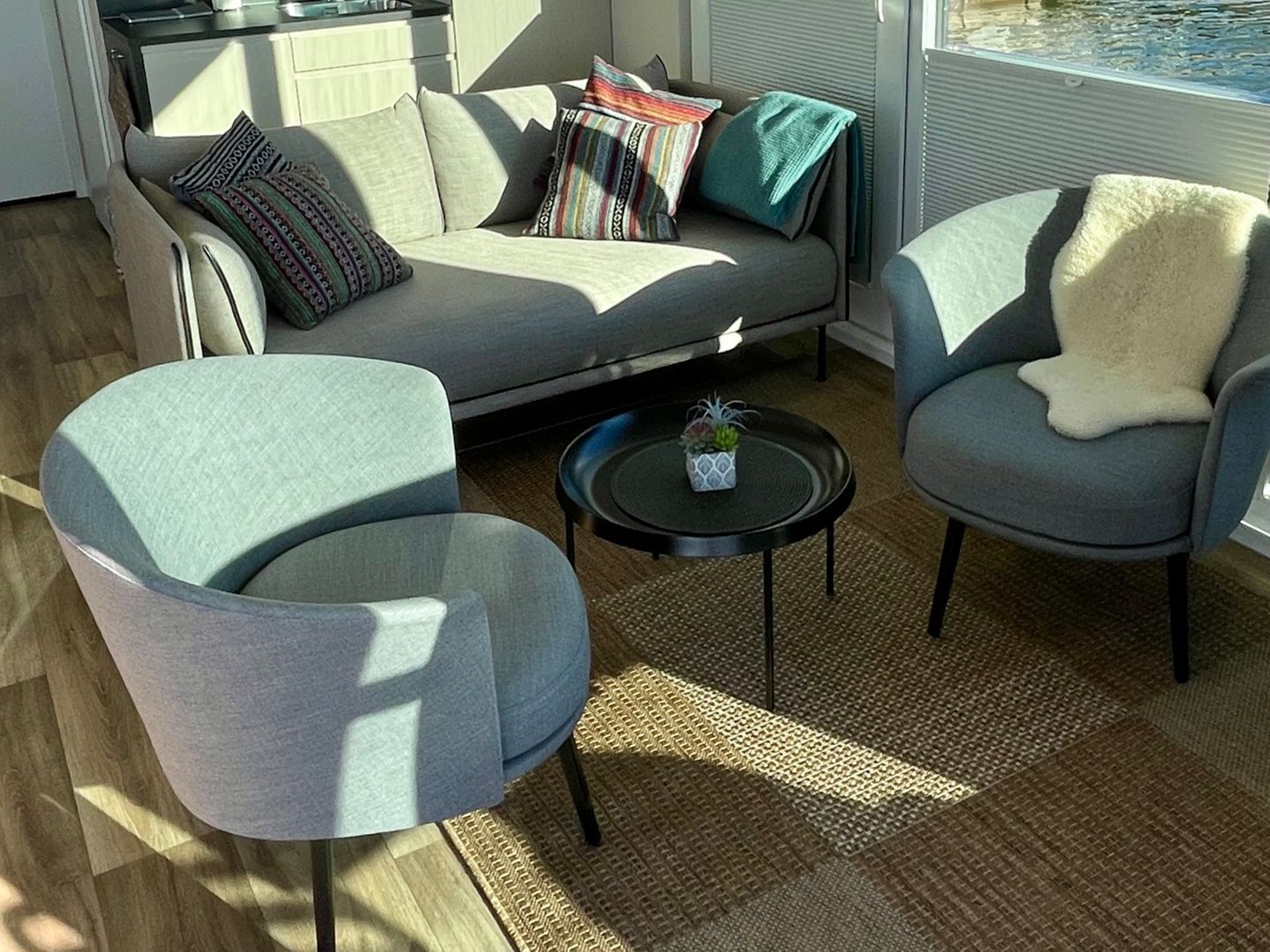 A modern living room with a sofa, two armchairs, a coffee table, and a small plant.