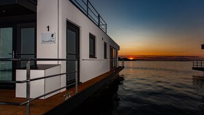 A modern boat with a white exterior, a deck with a railing, and a sign indicating room number 1. - Kranichnest Schwimmhaus - Kranichnest Schwimmhaus: lake view, terrace, wood-burning stove (Ribnitz-Damgarten)