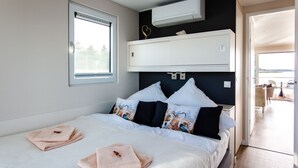 A modern bedroom with a bed, pillows, a window, an air conditioning unit, and a view of the outside. - Kranichnest Schwimmhaus - Kranichnest Schwimmhaus: lake view, terrace, wood-burning stove (Ribnitz-Damgarten)