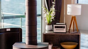 A modern room with a wood-burning stove, a potted plant, a radio, and a view of the sea. - Kranichnest Schwimmhaus - Kranichnest Schwimmhaus: lake view, terrace, wood-burning stove (Ribnitz-Damgarten)