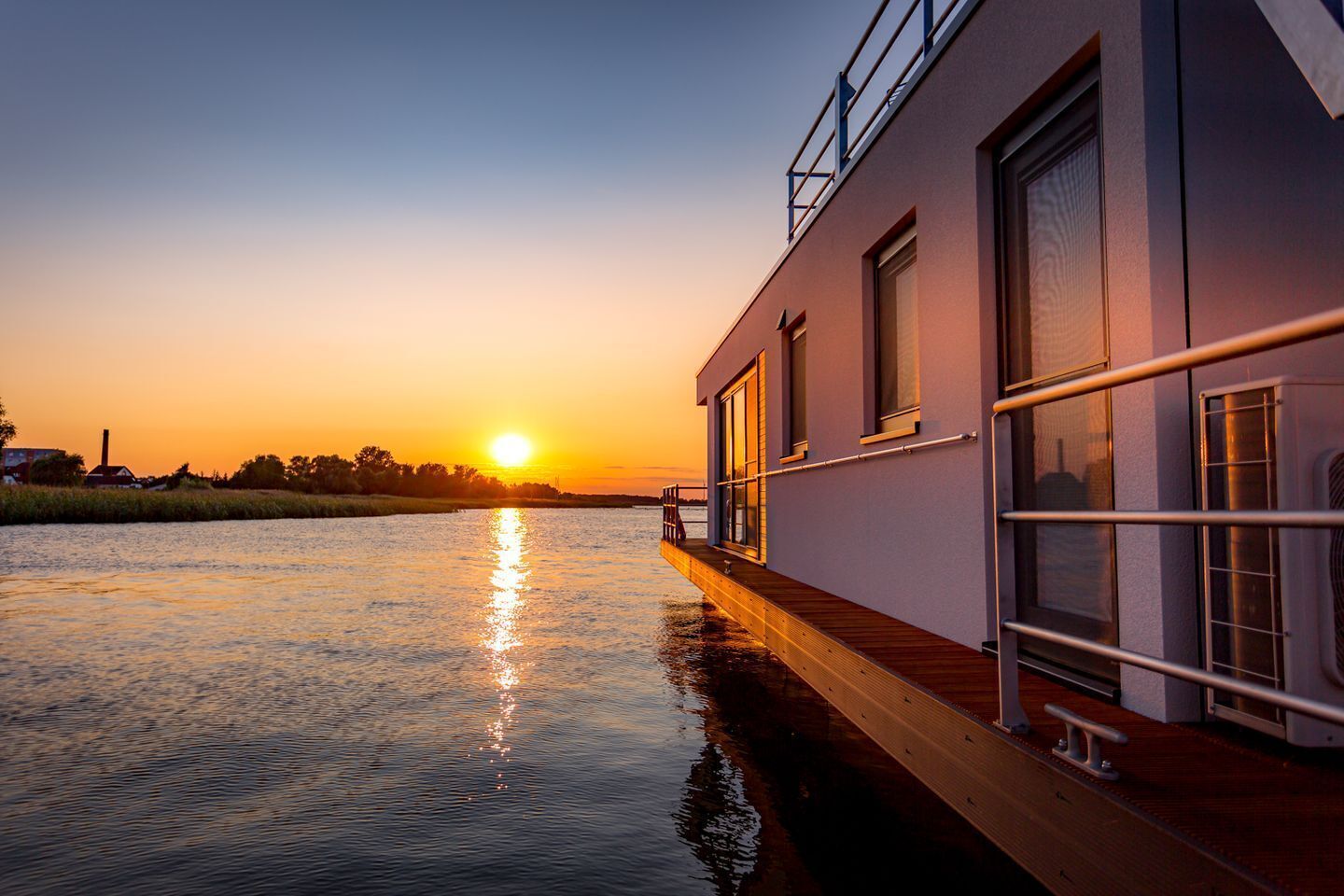 Een gebouw aan de rivier met een terras dat over het water uitsteekt, grote ramen en een hekwerk.