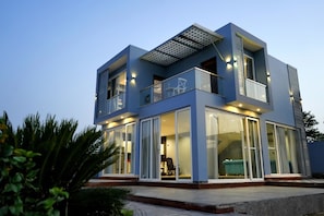 A modern two-story building with large glass windows, a balcony, and a flat roof with a skylight. - ELIVAAS Bluebell Villa 2 BHK Villa (Udaipur)