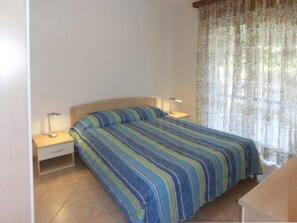 A bedroom with a bed, two bedside tables, a lamp on each, and a window with curtains. - Bright Retreat With Swimming Pool (Lignano Sabbiadoro)