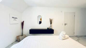 A minimalist bedroom with a bed, a dark console table, a mirror, and a door.