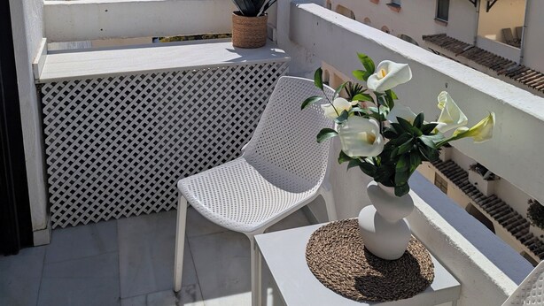 Un balcone con una sedia bianca, un tavolino e una pianta in vaso.