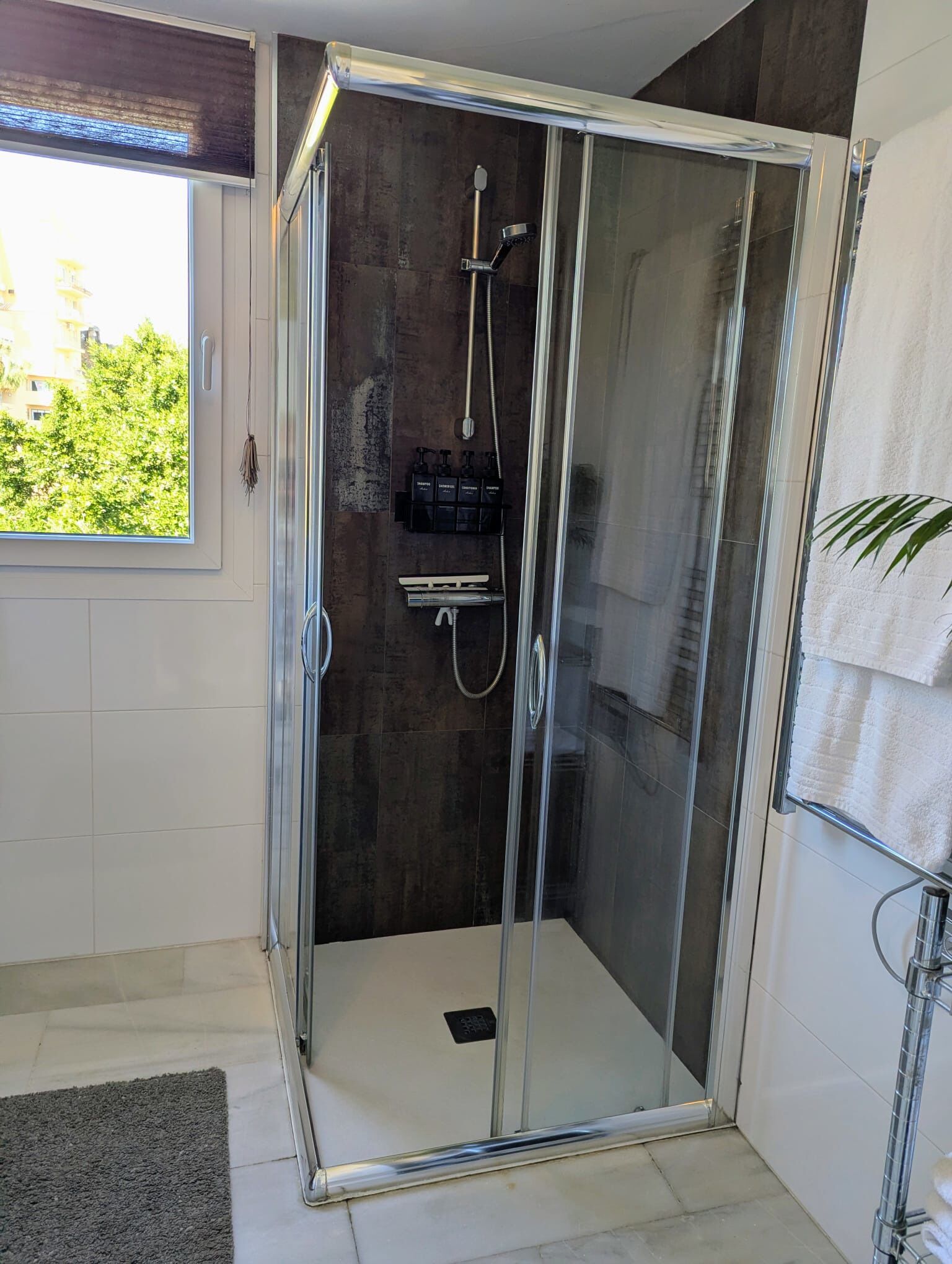 A glass-enclosed shower with a handheld showerhead and a wall-mounted faucet.