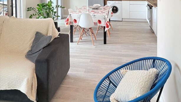 Ein zeitgemäßer Wohnbereich mit Sofa, Esstisch, Küchenzeile und blauem Sessel.