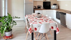 Eine moderne Küche mit weißen Schränken, einem Esstisch mit Blumen-Tischdecke und einem Blumentopf.
